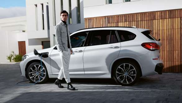 BMW hybride rechargeable X1 xDrive25e F48 vue de profil en charge BMW hybride rechargeable BMW X1 xDrive25e F48 LCI branchée à une borne de recharge, vue de profil avec mannequin