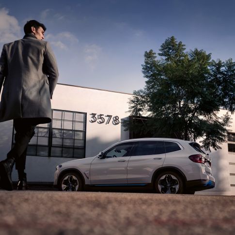 BMW iX3 G08, vue de profil devant un bâtiment avec homme BMW iX3 G08 2020 Mineralweiß metallic, vue de profil devant un bâtiment avec homme