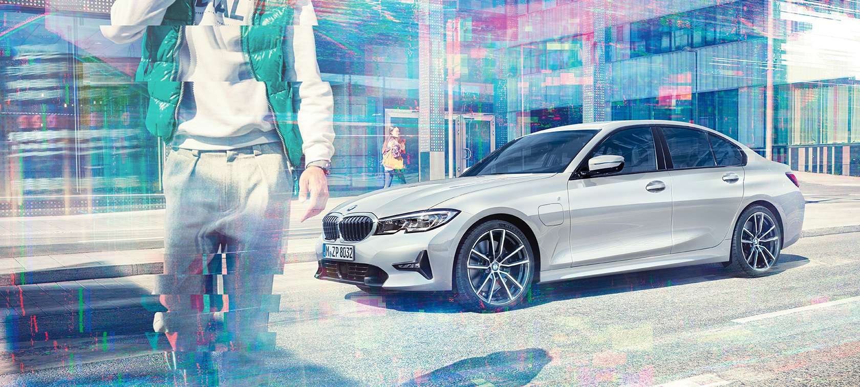 BMW Série 3 Berline, vue latérale BMW 330e. Vue de trois quarts latérale de la BMW 330e iPerformance Berline à l'arrêt devant un bâtiment en verre et passants dans une ville.