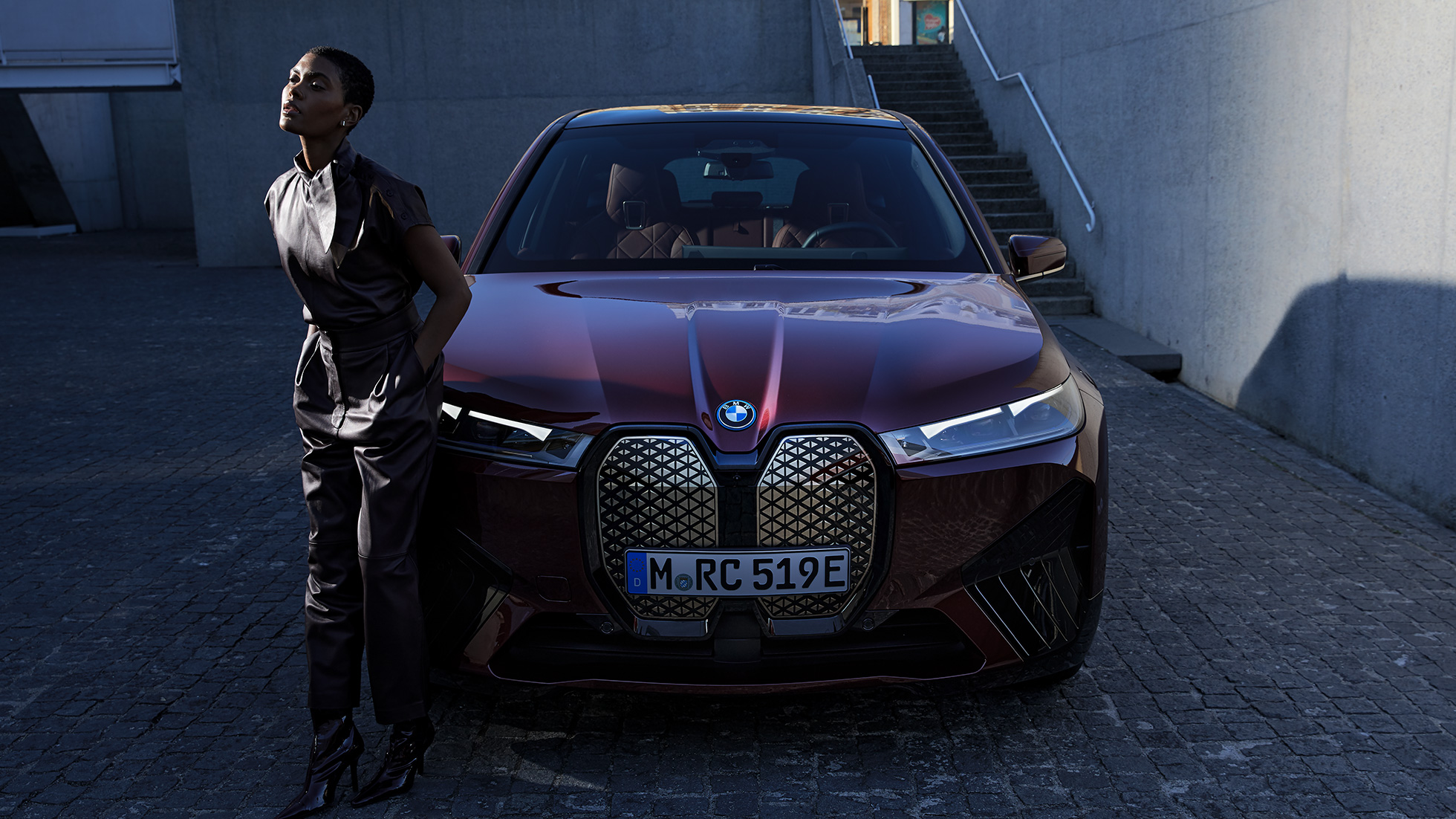 Vue avant de la BMW iX avec modèle Vue avant de la BMW iX Aventurinrot i20 avec modèle