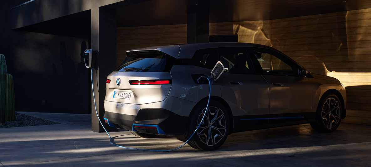 Vue de trois quarts arrière de la BMW iX branchée sur une BMW Wallbox BMW iX Kaschmirsilber i20, vue de trois quarts arrière, branchée à une BMW Wallbox