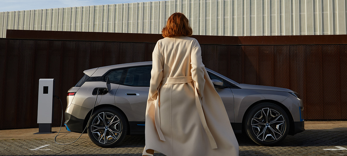 Vue latérale de la BMW iX à l'arrêt BMW iX Kaschmirsilber i20, vue de profil à l'arrêt avec modèle devant