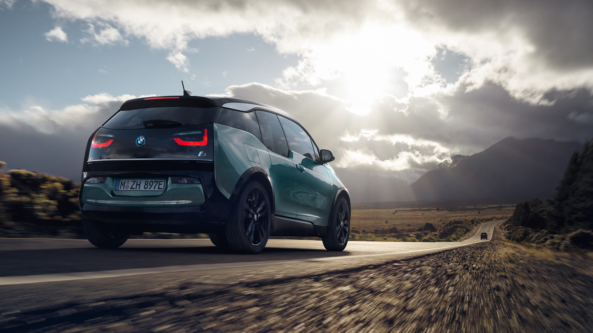 BMW i3 2018 vue de trois quarts arrière roulant sur une route de campagne BMW i3 I01 2018 Jucarobeige avec accent Frozen Grey metallic vue de trois quarts arrière roulant sur une route de campagne