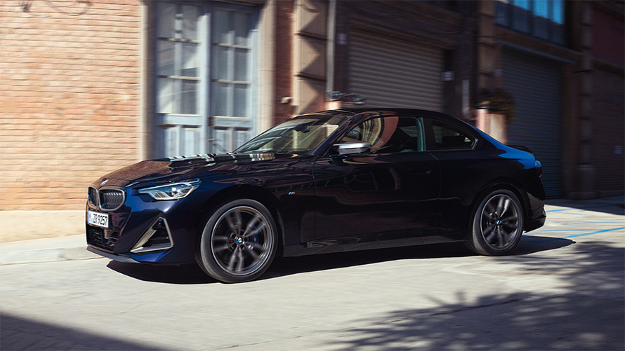 BMW M240i xDrive Coupé G42 2021 vue de profil à l’arrêt BMW M240i xDrive Coupé G42 2021 Black Sapphire metallic vue de profil devant entrepôt de stockage