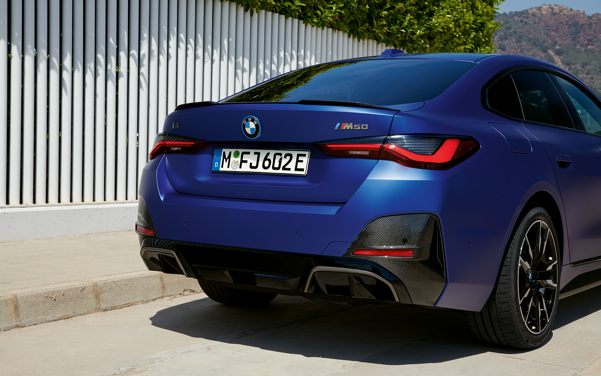 BMW i4 M50 G26 2021 BMW Individual Frozen Portimao Blau metallic vue de trois quarts arrière à l’arrêt près d’une clotûre blanche