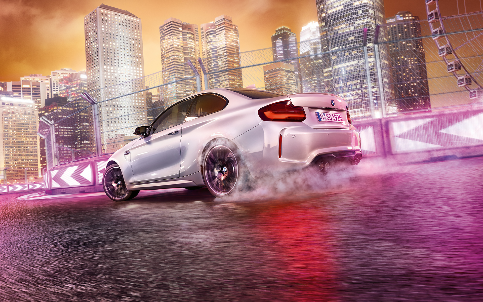 La BMW M2 Competition accélère. Une BMW M2 Competition blanche driftant sur le circuit de course, devant une skyline nocturne.
