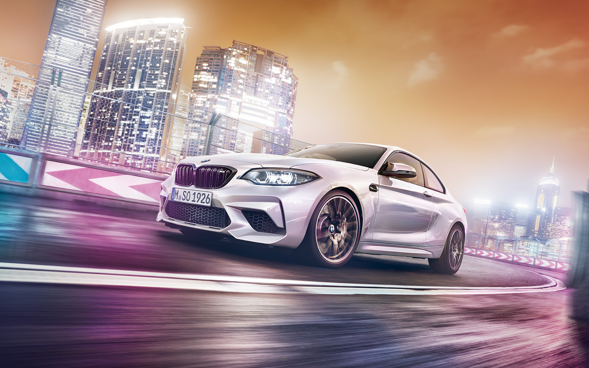 Une BMW M2 Competition blanche avec skyline. Une BMW M2 Competition blanche file sur le circuit de course devant une skyline nocturne.