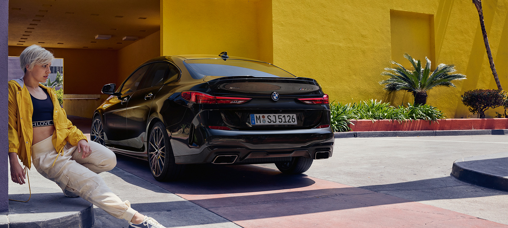BMW M235i xDrive Gran Coupé, vue de trois quarts arrière BMW M235i xDrive Gran Coupé Black Sapphire metallic F44, vue de trois quarts arrière avec femme au premier plan