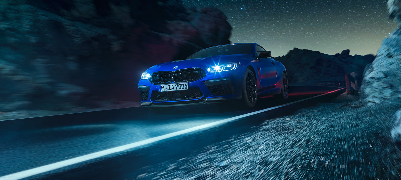 BMW M8 Competition Coupé, vue de trois quarts avant. La première BMW M8 Competition Coupé en Marina Bay Blau metallic, vue de trois quarts avant, en marche, de nuit.
