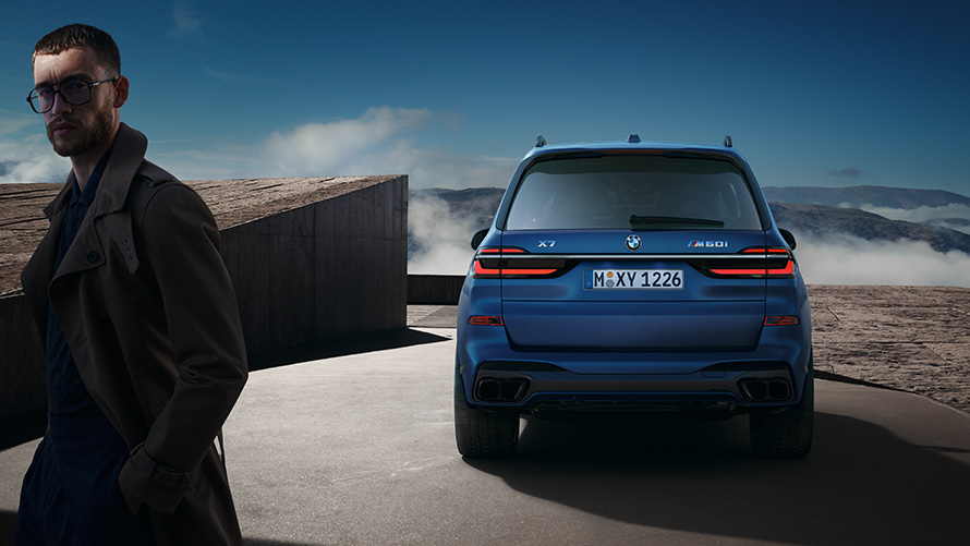 BMW X7 M60i xDrive G07 LCI Frozen Marina Bay Blue vue arrière à l'arrêt devant un paysage de montagnes avec modèle