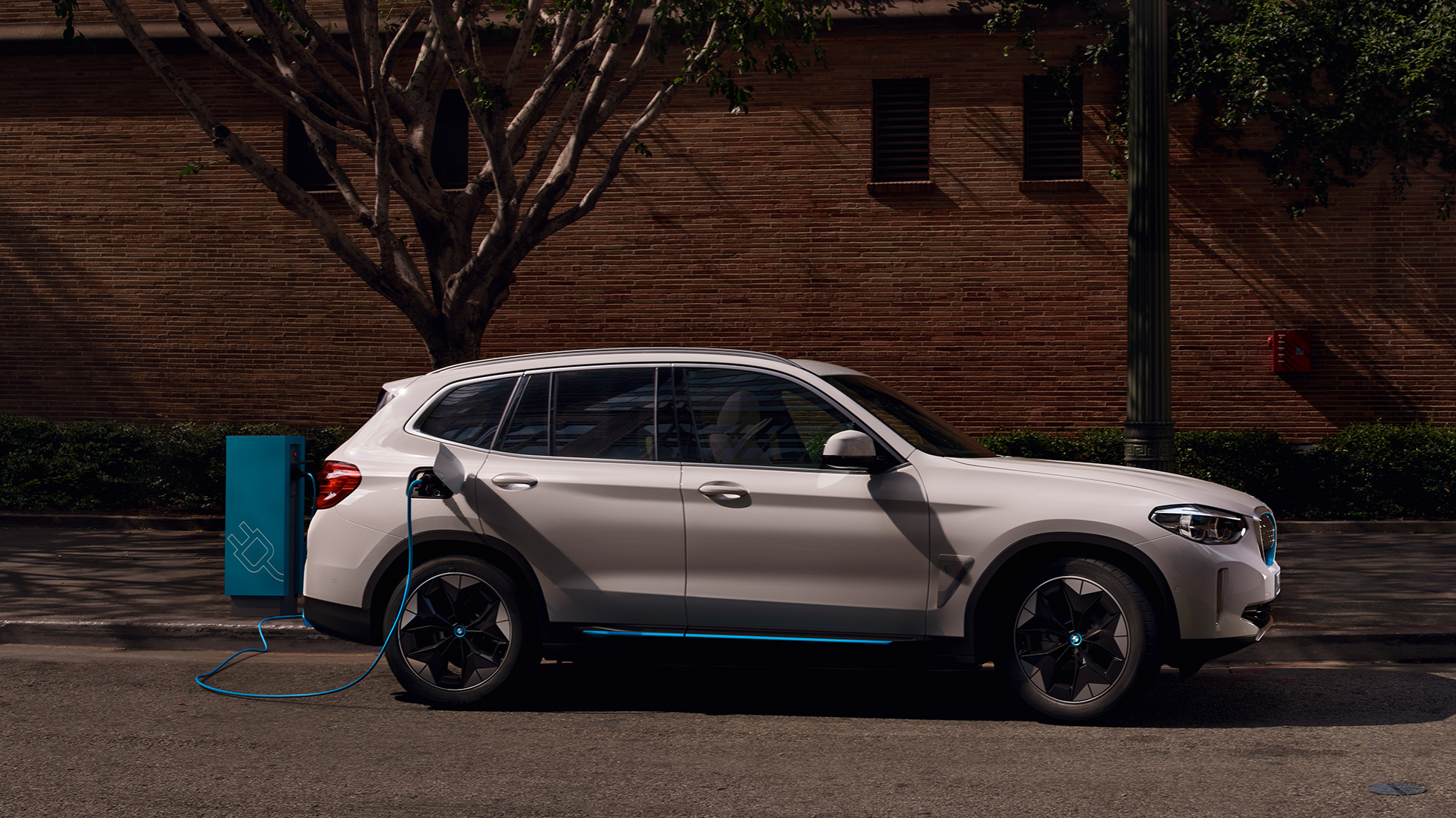 High Power Charging BMW iX3 G08 sur une borne de recharge publique, vue de profil High-Power Charging BMW iX3 G08 2020 Mineralweiß metallic sur une borne de recharge publique, vue de profil
