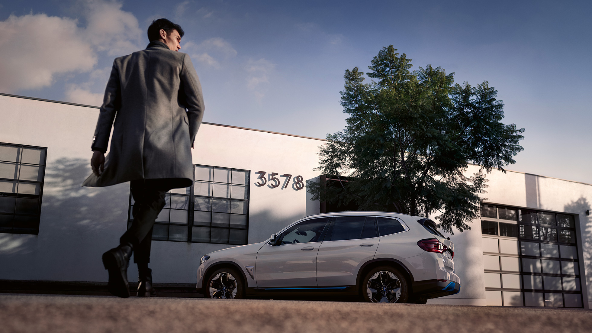 BMW iX3 G08, vue de profil devant un bâtiment avec homme BMW iX3 G08 2020 Mineralweiß metallic, vue de profil devant un bâtiment avec homme