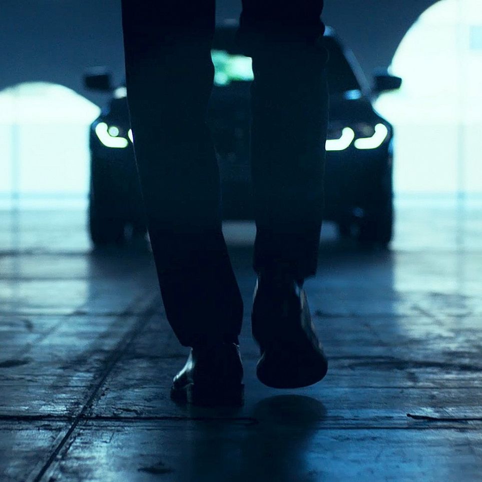 Avant de la BMW Série 3 Berline. Vue de l’arrière d’un homme marchant devant la BMW Série 3 Berline sur l’asphalte.
